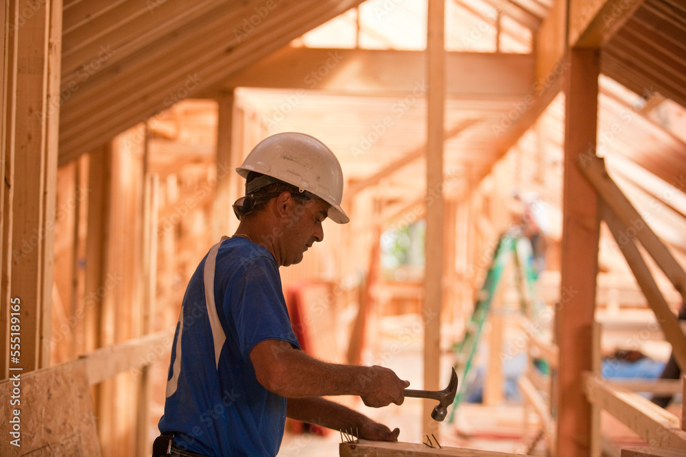 Hispanic carpenter hammering nails on board at a house under construction Hispanic carpenter hammering nails on board at a house under construction