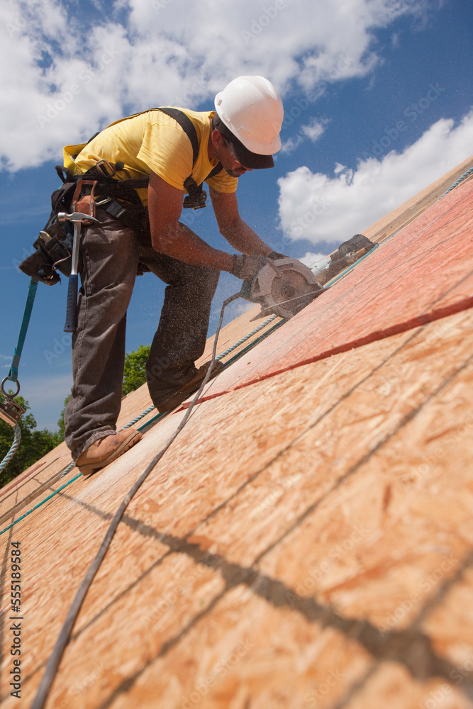 Carpenter using a circular saw on the roof panel at a house under construction site Carpenter using a circular saw on the roof panel at a house under construction site