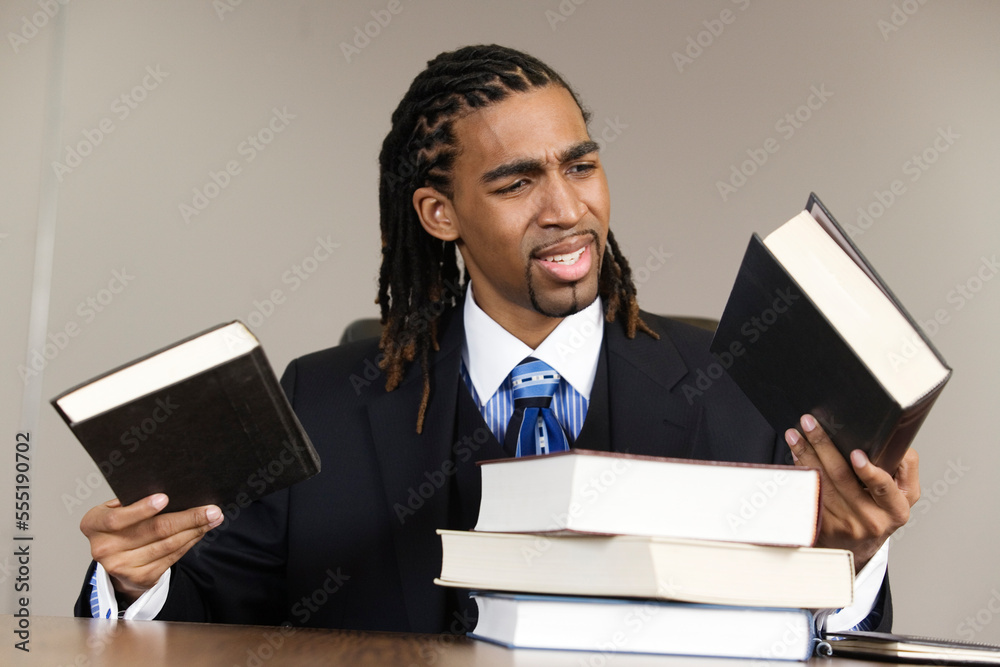 A confused young business man holding books in an office. A confused young business man holding books in an office.