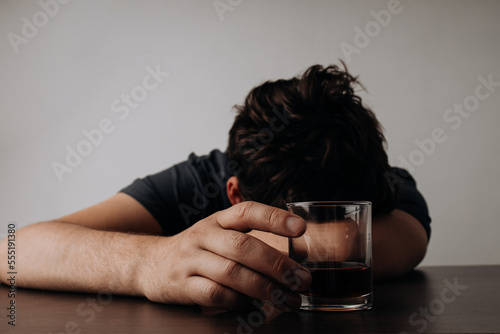 Alcoholism, depressed man sleep on table while drinking alcoholic beverage, holding glass of whiskey photo
