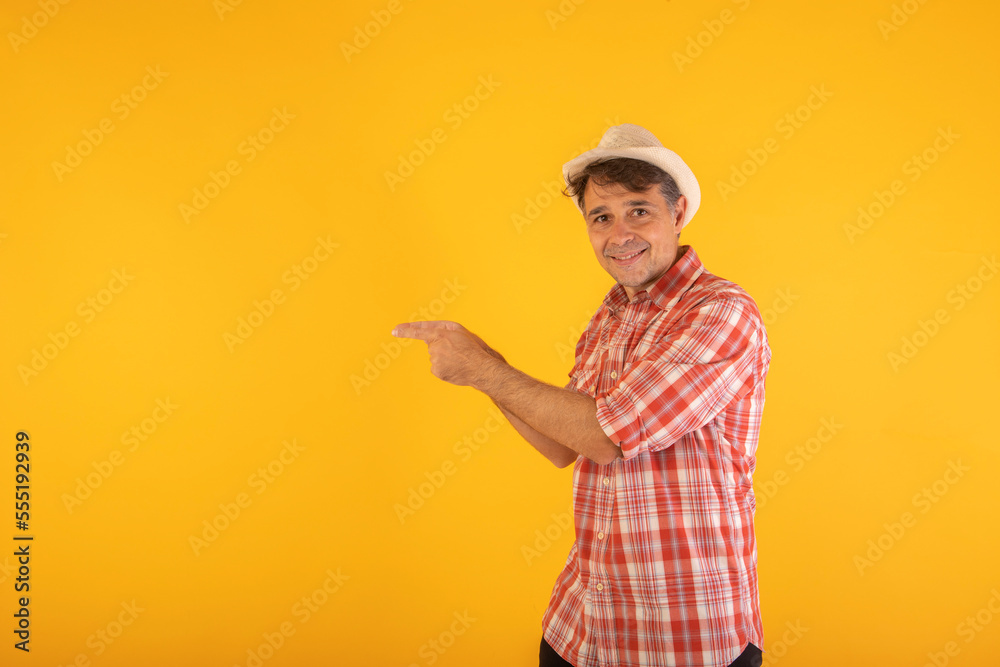 Man in hat and colorful checkered shirt pointing to the side with his hands on an orange background Man in hat and colorful checkered shirt pointing to the side with his hands on an orange background