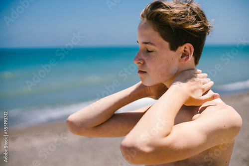 Boy applies sun screen on sunny day at beach with blue ocean