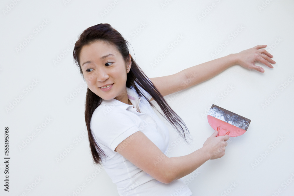 Side profile of a young woman scraping paint on wall Side profile of a young woman scraping paint on wall