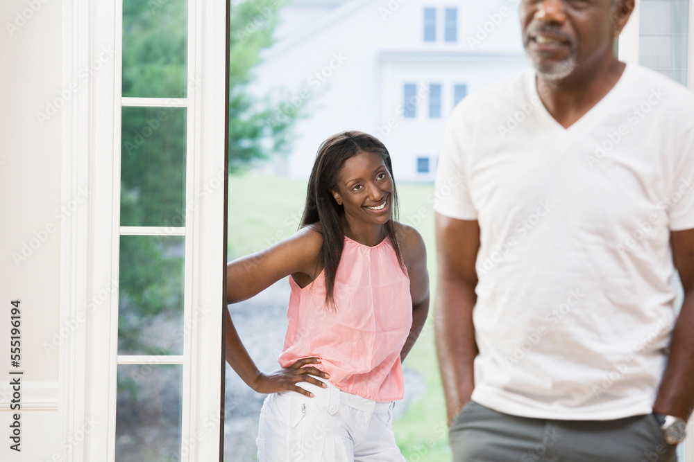 Middle-aged woman standing at a doorway smiling with arms akimbo and looking at a middle-aged man Middle-aged woman standing at a doorway smiling with arms akimbo and looking at a middle-aged man
