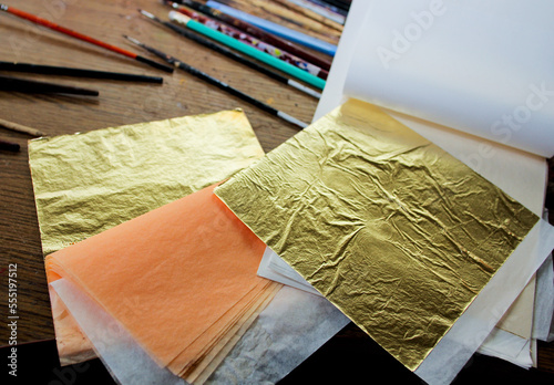 Gold Leaf. A lot of square gold leaf in studio of painter. Brushes and pencils on the background. photo