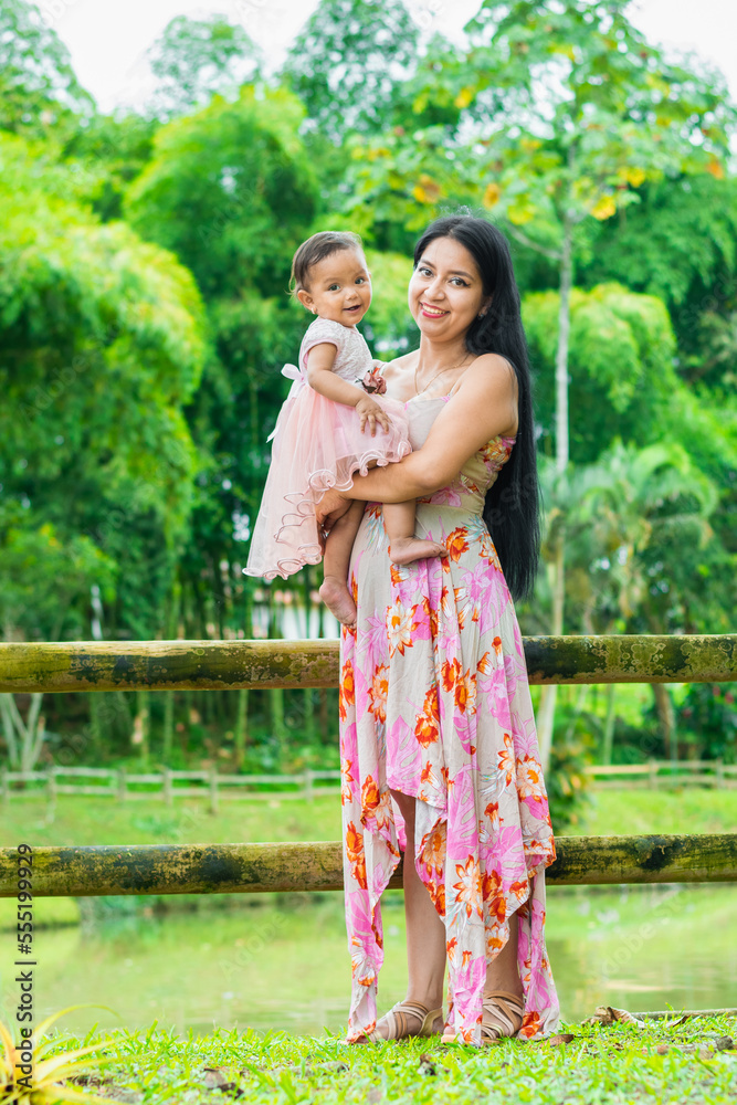 portrait of latin woman holding her baby who is happy to have her by her side. in the background green nature. concept of healthy motherhood.