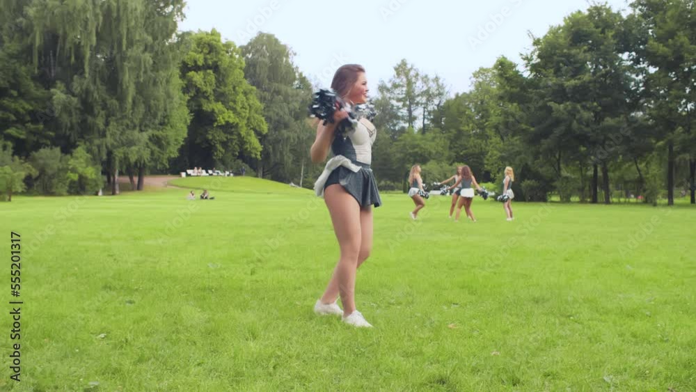 Girl cheerleader in suit is exercising with big pom-poms in park. Realtime Girl cheerleader in suit is exercising with big pom-poms in park. Realtime