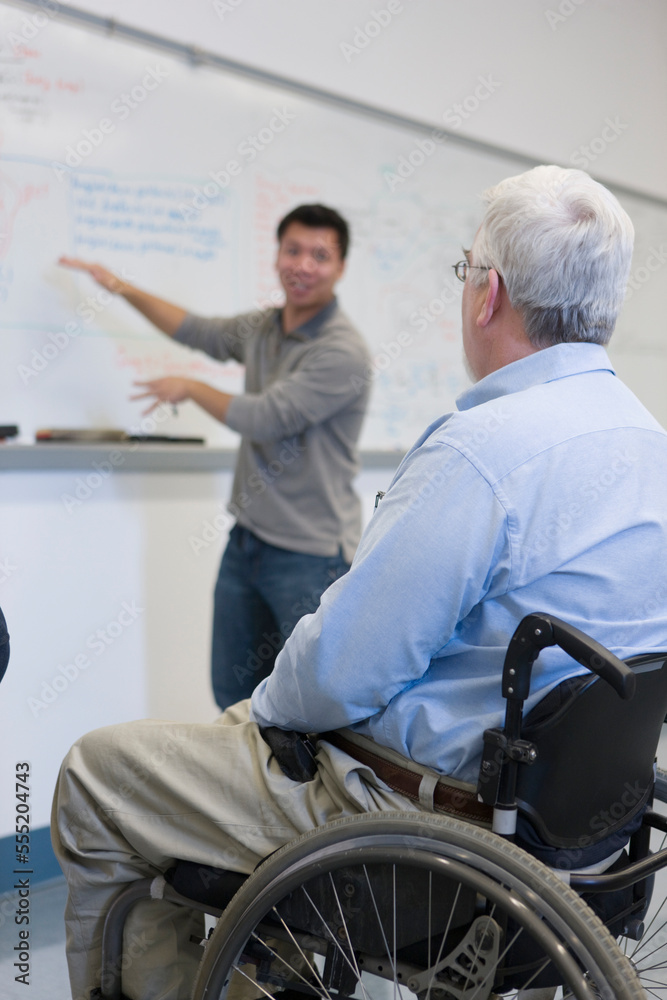 Student explaining to professor with Muscular Dystrophy in a classroom Student explaining to professor with Muscular Dystrophy in a classroom