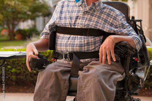 Man with Duchenne muscular dystrophy sitting in a motorized wheelchair using power controller with degenerated hands photo