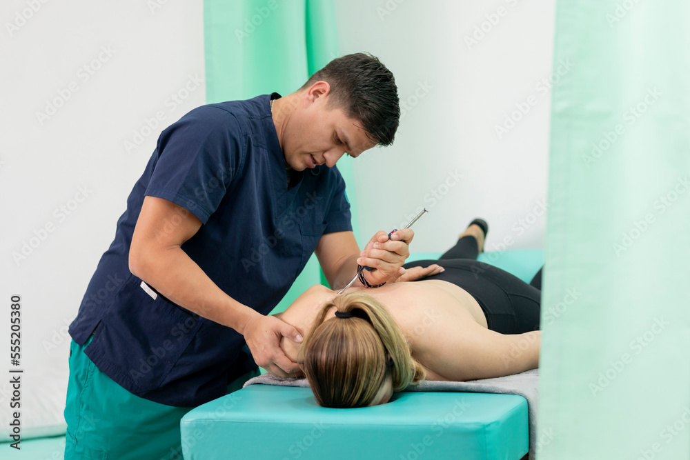 Obraz premium Latino physiotherapist doctor applies a treatment for Fibrolysis to his female patient, lying face down on the table