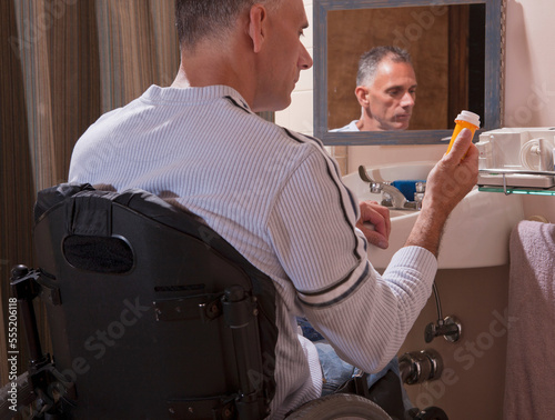 Man with spinal cord injury in a wheelchair looking at a pill bottle photo