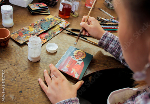 For protection wooden picture is process of applying сraquelure varnish on the product. Reproduction of the icon of St. Nicholas. Workflow of the artist in the studio. Brushes and paints on the backgr photo
