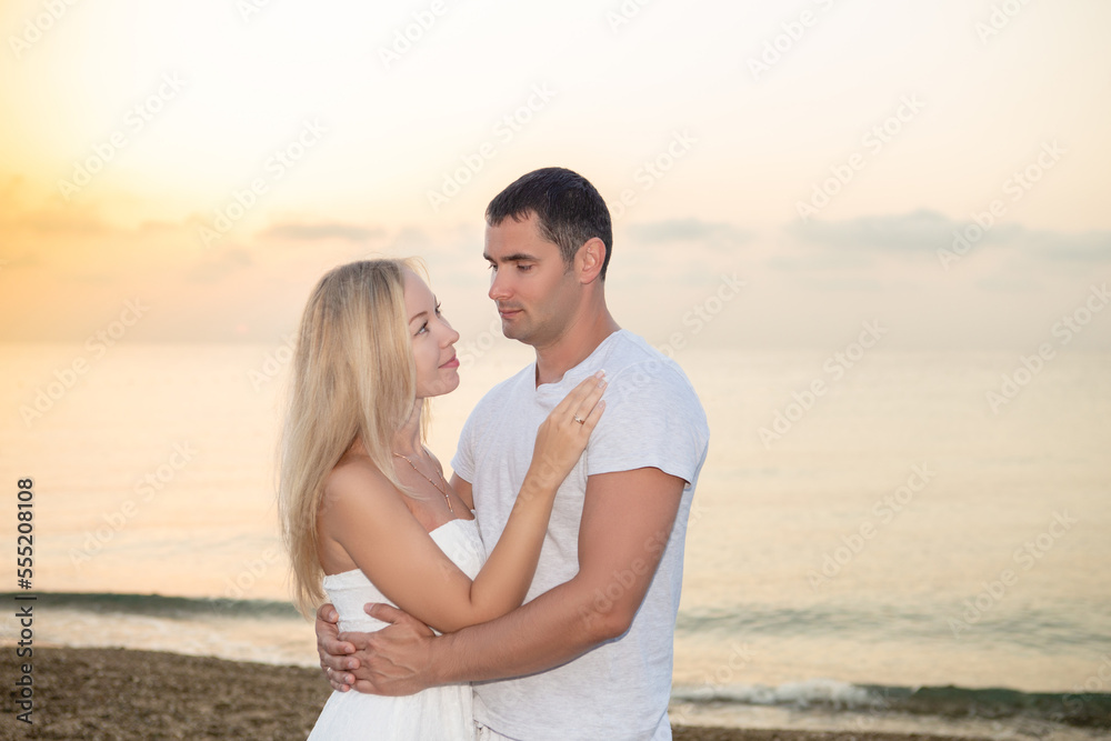 Young couple on the background of the sea sunset or sunrise. Young woman and young brunette man on the sea shore of pebbles. Young couple on the background of the sea sunset or sunrise. Young woman and young brunette man on the sea shore of pebbles.