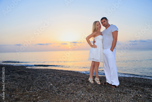 Young couple on the background of the sea sunset or sunrise. Young woman and young brunette man on the sea shore of pebbles.
