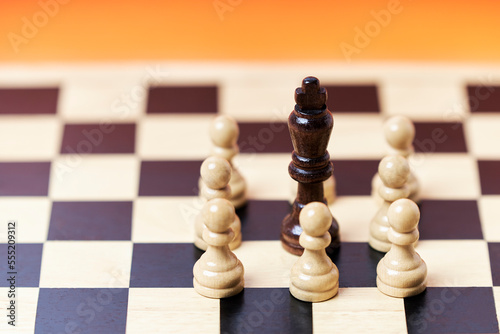 Chess group of white pawns with black king challenge center on orange background
