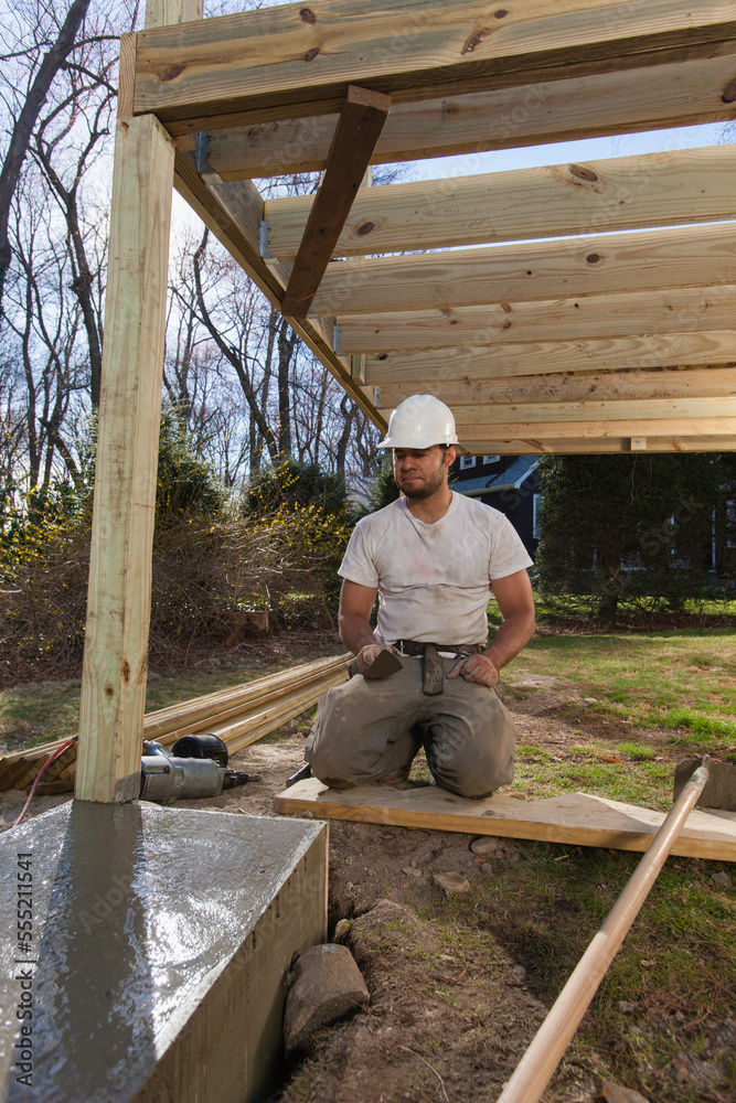 Hispanic carpenter with trowel inspecting deck footing