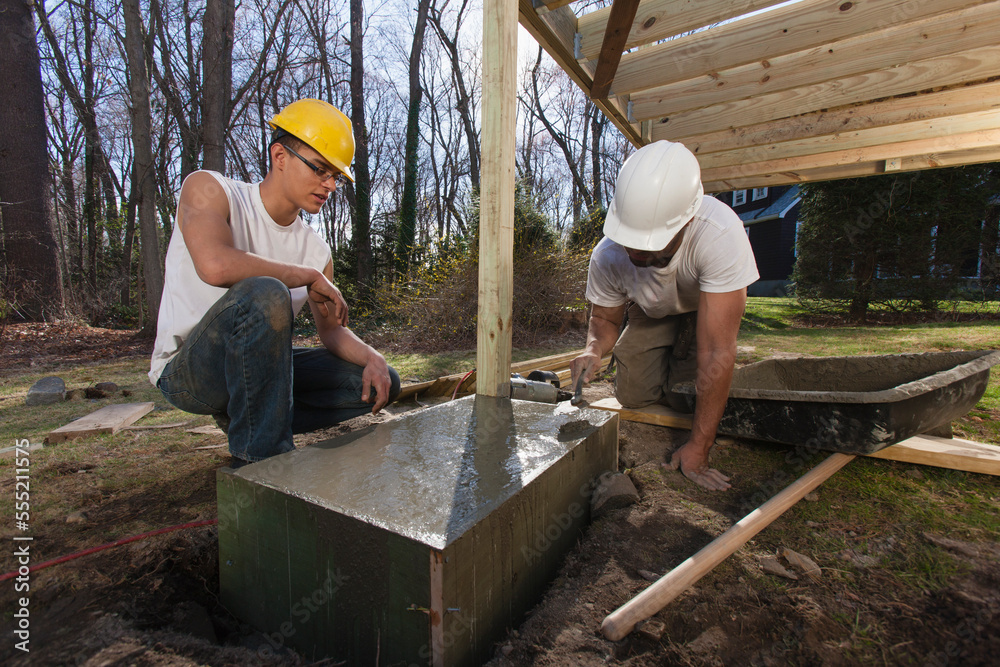 Hispanic carpenters using trowel to smooth concrete for staircase footing Hispanic carpenters using trowel to smooth concrete for staircase footing