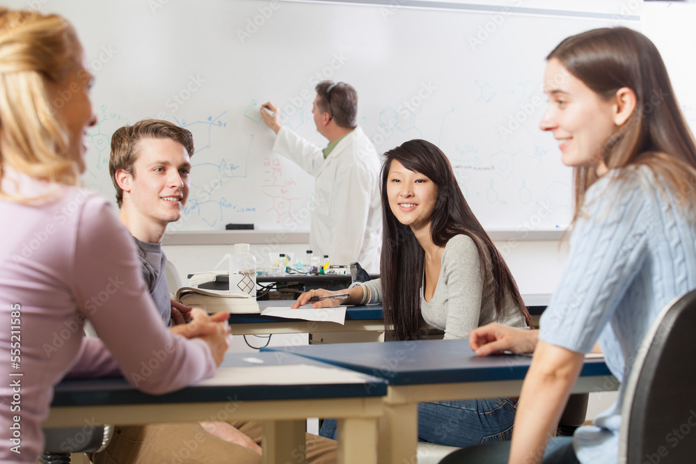 Students talking in an engineering class while the professor is writing on the white board
