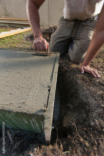 Hispanic carpenter using finish trowel to roughen stairway footing concrete