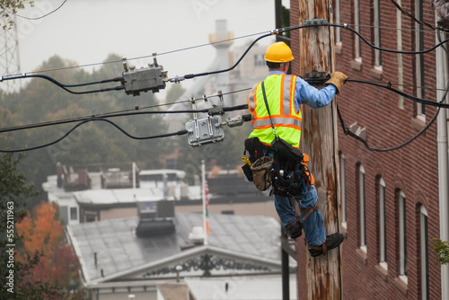 Cable lineman using lineman spikes to climb down pole photo