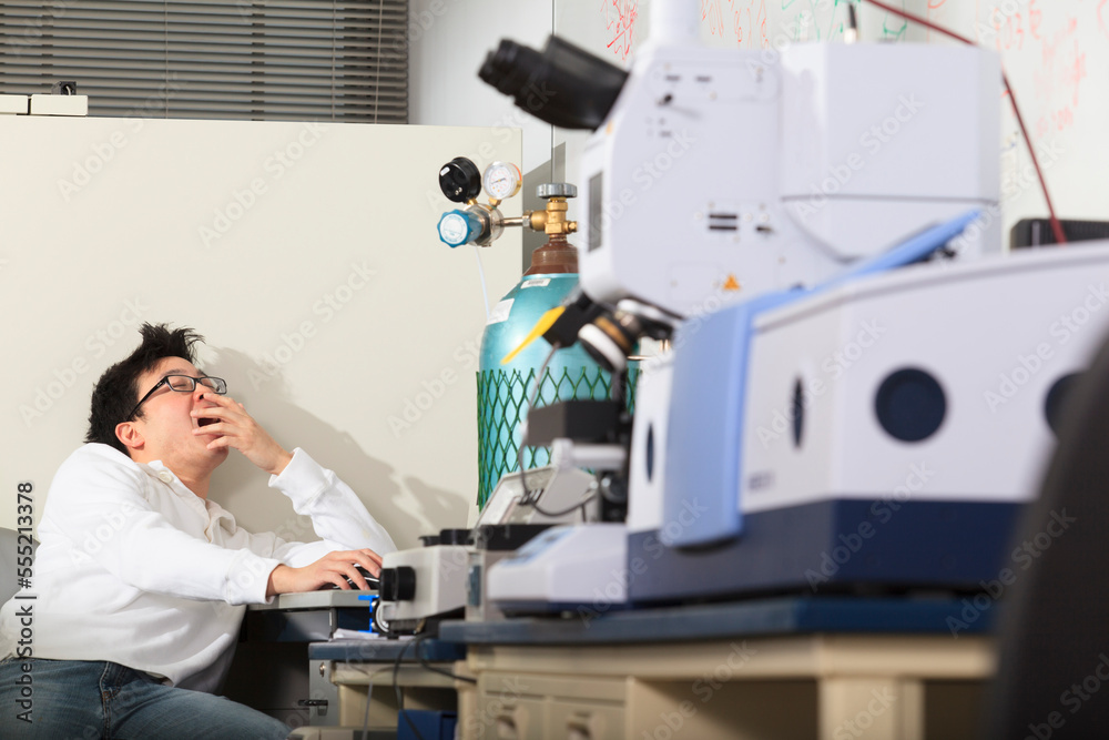 Engineering student using keyboard for chemical analysis instrument and yawning in a laboratory Engineering student using keyboard for chemical analysis instrument and yawning in a laboratory