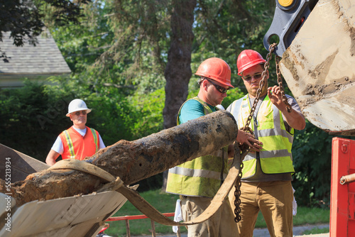 Construction workers unhooking old watermain from excavator photo