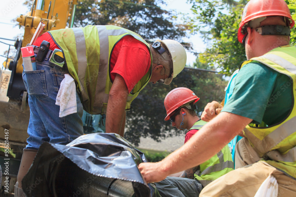 Construction workers preparing for excavator to lift water main into place Construction workers preparing for excavator to lift water main into place