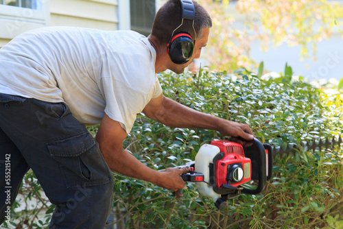 Landscaper trimming bushes with an electric trimmer