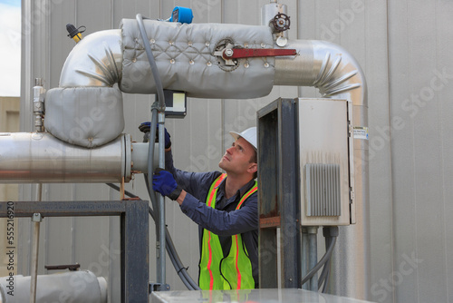 Industrial engineer reading a transducer display on insulated high pressure pipe in a power plant