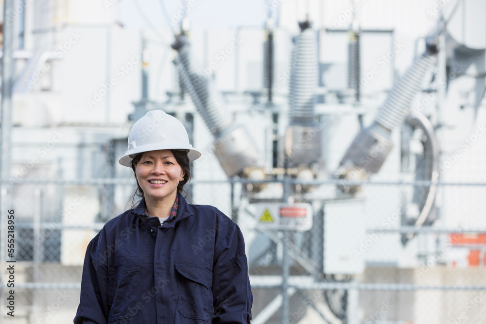 Portrait of female power engineer in front of high voltage transformer at power station Portrait of female power engineer in front of high voltage transformer at power station