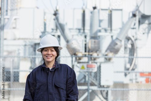 Portrait of female power engineer in front of high voltage transformer at power station photo