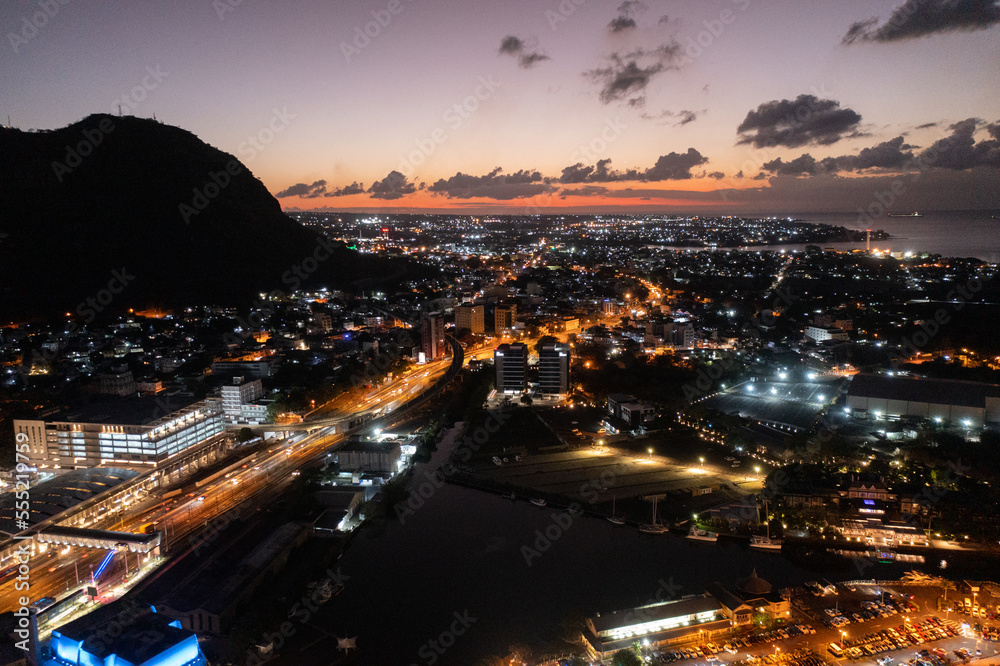 Aerial night view of the old and modern buildings at Waterfront in Port Louis, Capital of Mauritius with  Bird eyes view during nighttime, with illuminated buildings in front and dark mountain scenery