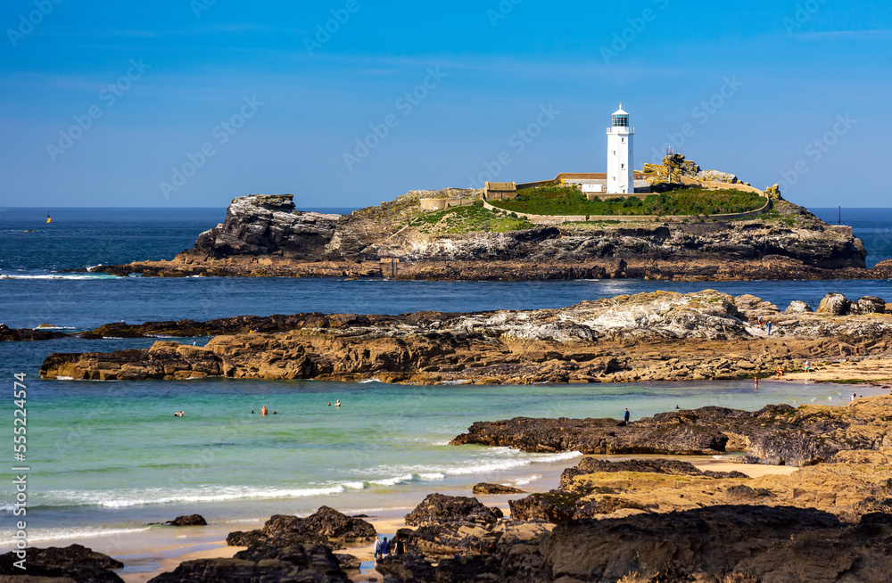 White Godrevy Lighthouse on rock formation in blue water with blue sky and rocky shoreline, Godrevy Island in St. Ives Bay; Cornwall County, England White Godrevy Lighthouse on rock formation in blue water with blue sky and rocky shoreline, Godrevy Island in St. Ives Bay; Cornwall County, England