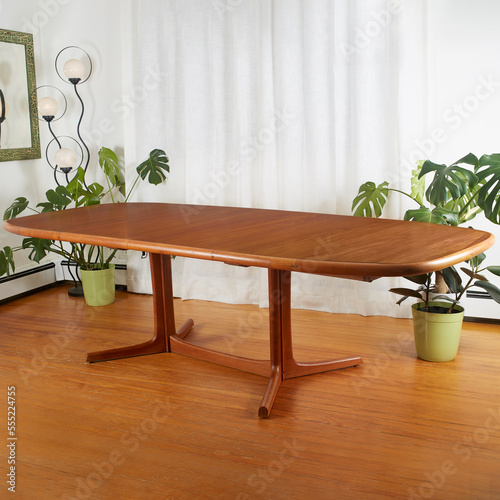 Table, mid-century modern dining room piece. Warm teak wood vintage furniture. Scene with white curtains, houseplants, and a dynamic retro- futurist lamp.