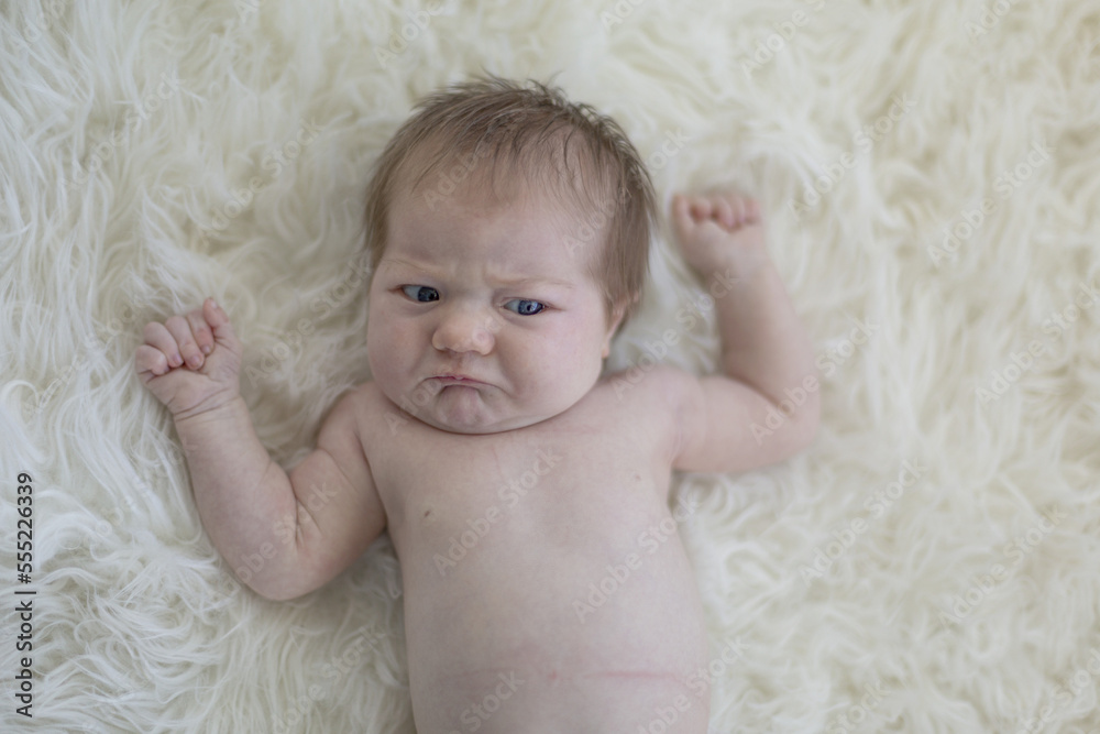 An infant girl lays on a white fur rug making a sad face and about to cry; Studio An infant girl lays on a white fur rug making a sad face and about to cry; Studio