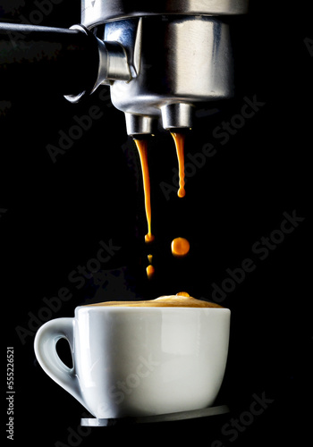 Close up of espresso coffee machine dripping coffee into white espresso cup with foam on surface of cup; Studio