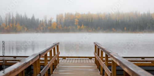 Dock on Hush Lake with fog blurring the autumn coloured forest along the shoreline; British Columbia, Canada photo