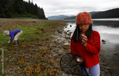 Two girls beach-comb near the water's edge investigating crabs and other sea life at low tide in the intertidal zone of Southeast Alaska; Inside Passage, Alaska, United States of America