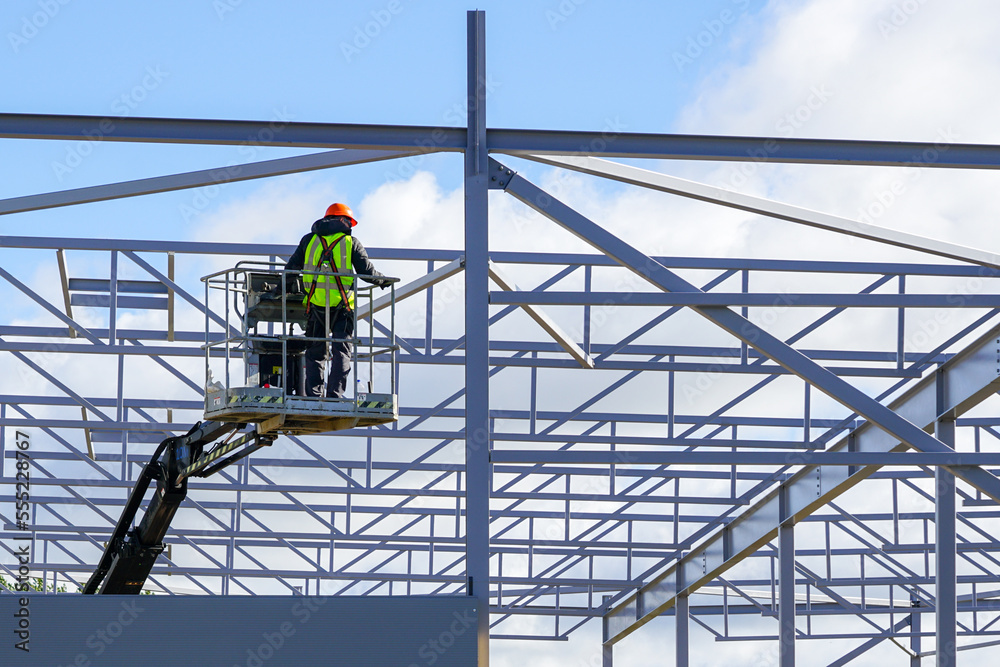Worker in self propelled mobile crane basket in uniform on a building steel framework background