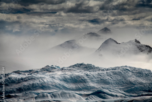 Iceberg in the foreground acts like a stage for wind-whipped snow blowing past mountains lining Iceberg Alley on the way to the western Antarctica Peninsula; Antarctica photo