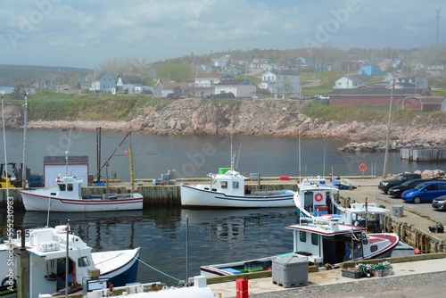 Foggy view of Neil's Harbor with docked boats and homes in the distance.; Neil's Harbor, Cape Breton Highlands National Park, Nova Scotia, Canada.