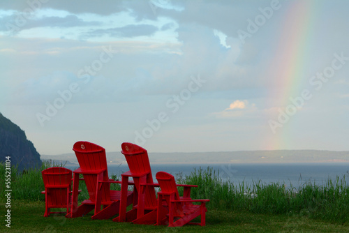 Adirondack chairs facing the Bay of Fundy with a rainbow in the sky.; Alma, Fundy National Park, New Brunswick, Canada.