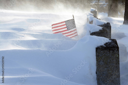 A United States of America flag flying at a veteran's gravestone during a record blizzard in 2015.; Mount Pleasant Cemetery, Arlington, Massachusetts. photo