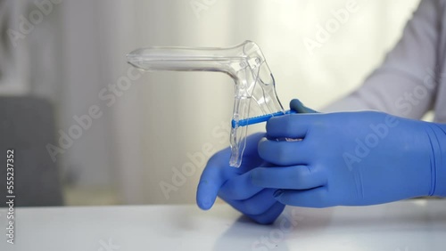 Close-up hands of gynecologist in gloves holding cusco vaginal speculum. Unrecognizable Caucasian man sitting at table in hospital with gynecological instrument photo