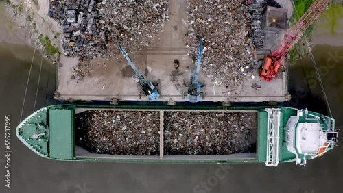 Cranes working simultaneously to load cargo ship with scrap metal at a tidal river port 4K