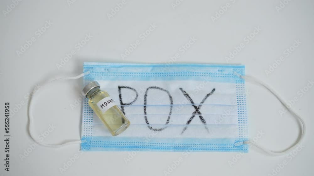 Close-up pox written on face mask with monkeypox vaccine. Top view virus infection protection on white table. Slow motion