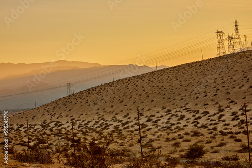 Electrical power lines carrying clean energy across desert hills at sunset during the golden hour