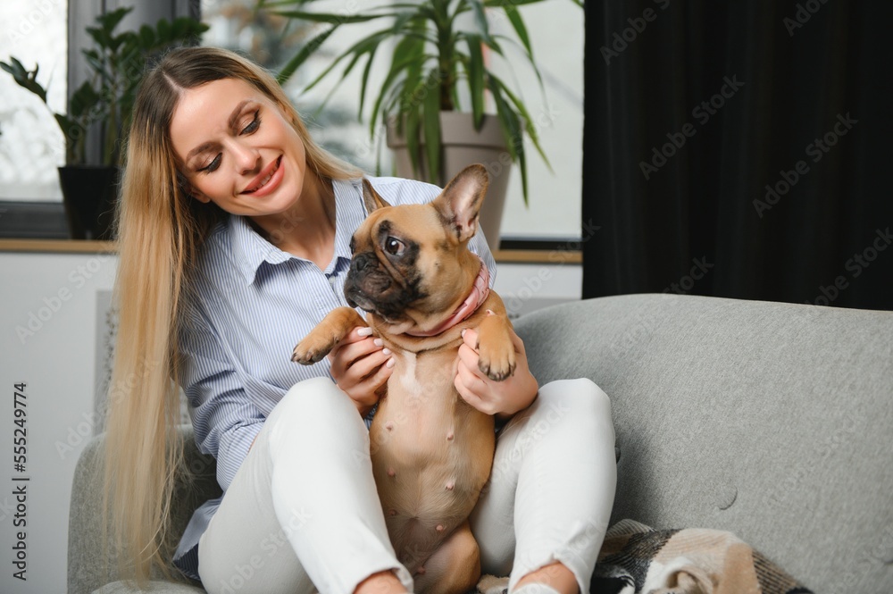 Beautiful redhead woman sitting on a sofa laughing and cuddling a dog Beautiful redhead woman sitting on a sofa laughing and cuddling a dog