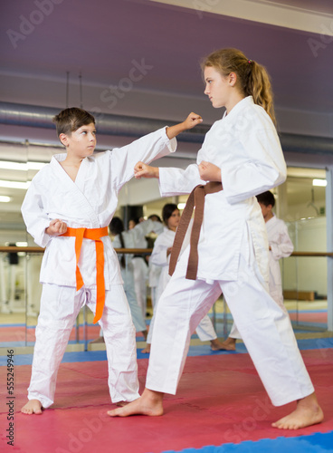 Boy and girl sparring together during group karate training in gym.