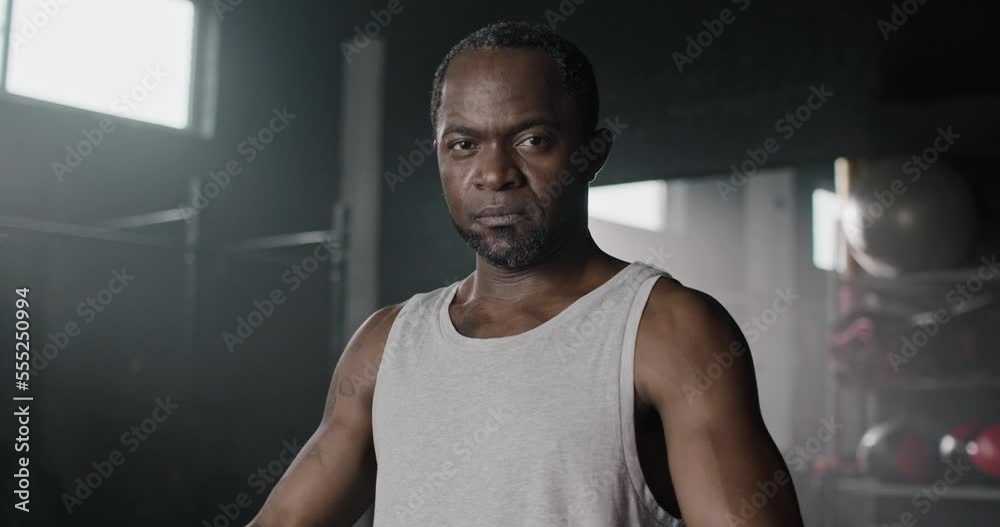 Close-up portrait of beautiful muscular powerful professional African fighter standing in gym in top tank wearing boxing bandages looking at camera. Serious focused African-American male boxer. Close-up portrait of beautiful muscular powerful professional African fighter standing in gym in top tank wearing boxing bandages looking at camera. Serious focused African-American male boxer.